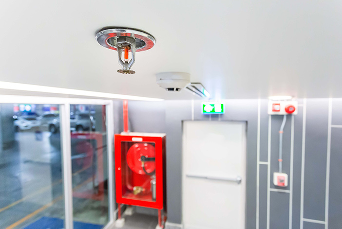 Ceiling-mounted sprinkler overlooking fire alarm, an emergency exit and fire hose