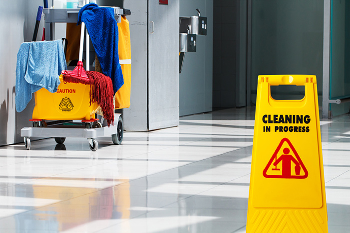 A Cleaning In Progress floor sign beside a trolley of cleaning equipment