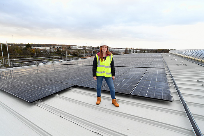 Abigail Beasley stood on a roof covered in Solar Panels