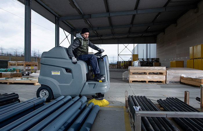 A man cleaning an outside warehouse area with a Kärcher Hire ride-along floor cleaner