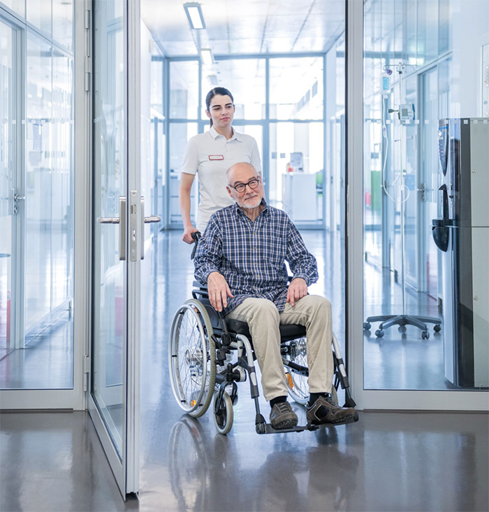 A nurse pushing a man in a wheelchair through an open door